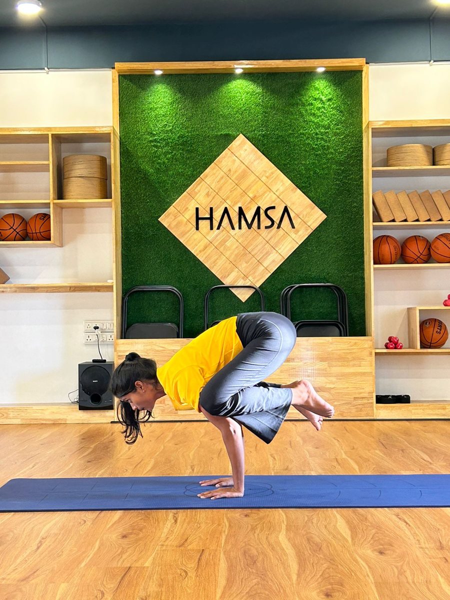 Instructor holding Crow pose in front of the Hamsa studio wall